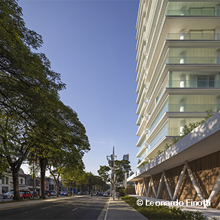 Foto da sala de leitura do edifício Float. No primeiro plano, há dois sofás brancos. No segundo plano, há uma estante de livros. Atrás, a parede de vidro mostra a vegetação do fundo.